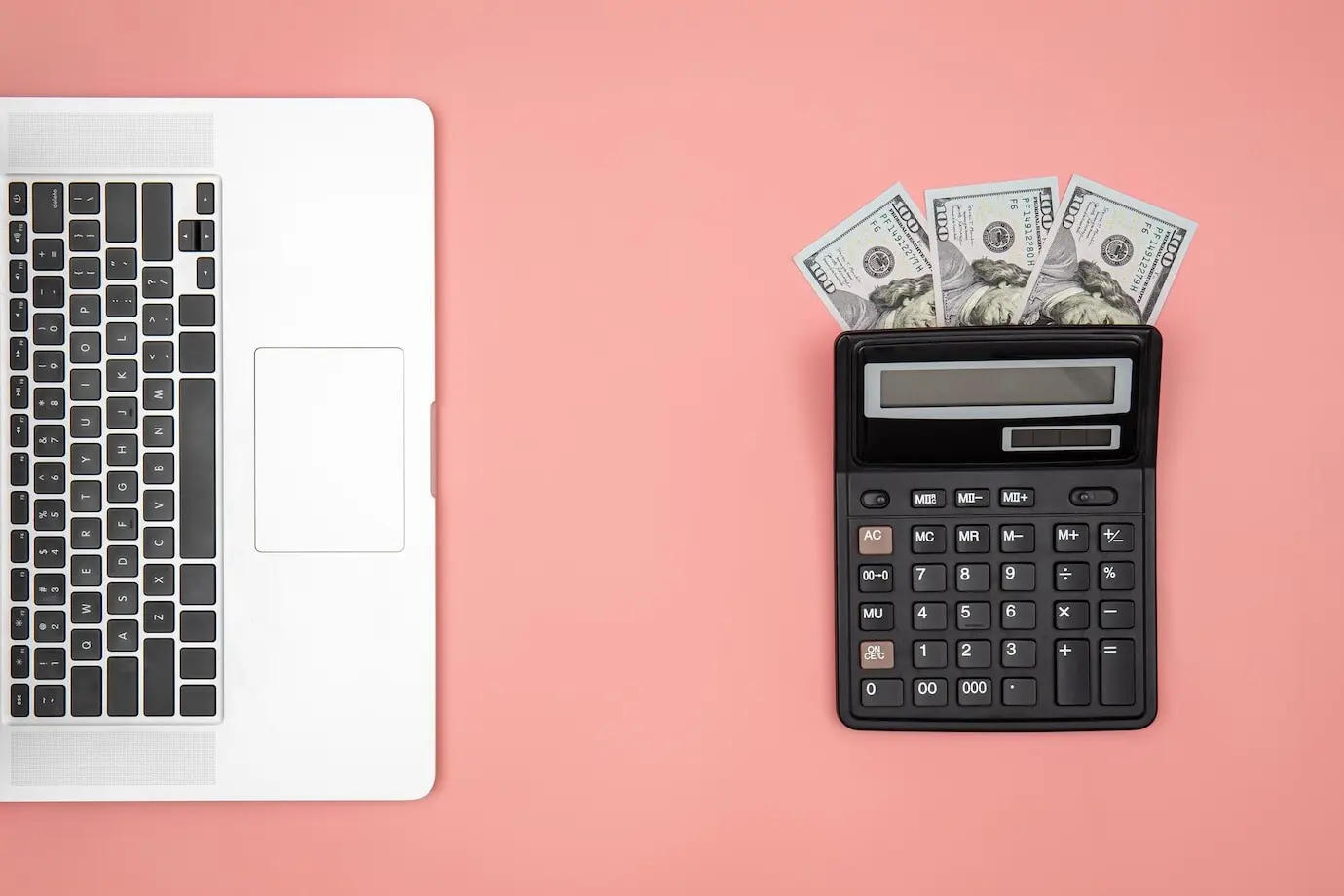 A flat lay of a calculator, a laptop, and dollar bills on a colored background.